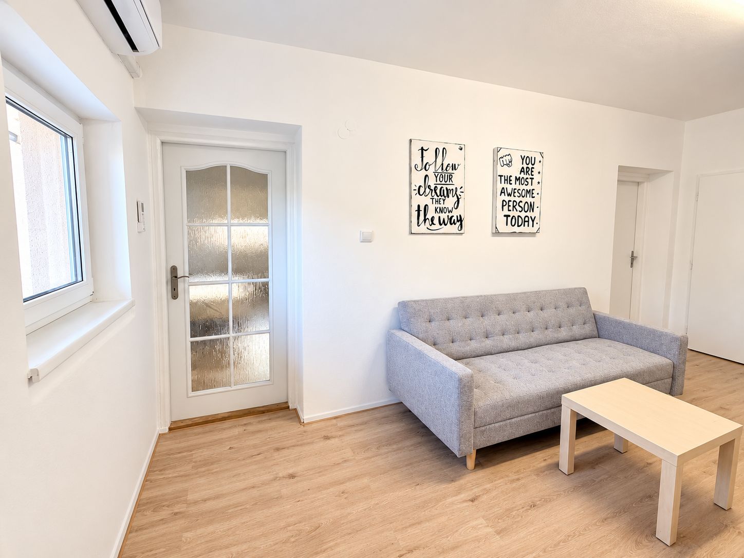 A room with a grey sofa, a wooden coffee table, and two motivational wall art pieces.