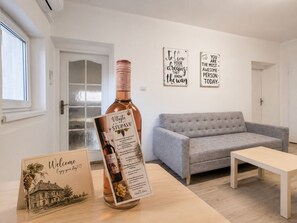 Un saló modern amb un sofà gris, una taula de centre de fusta i una ampolla de vi Stupave. Hi ha dues obres d'art motivacional a la paret i una targeta de benvinguda amb una il·lustració d'una vinya.