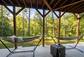 A covered outdoor seating area with two hammocks and a small table, surrounded by a forest. - 5-BR 4-BA Modern Rustic house on 5.5 acres. 25-30 min from Blue Ridge or Ellijay (Cherry Log)