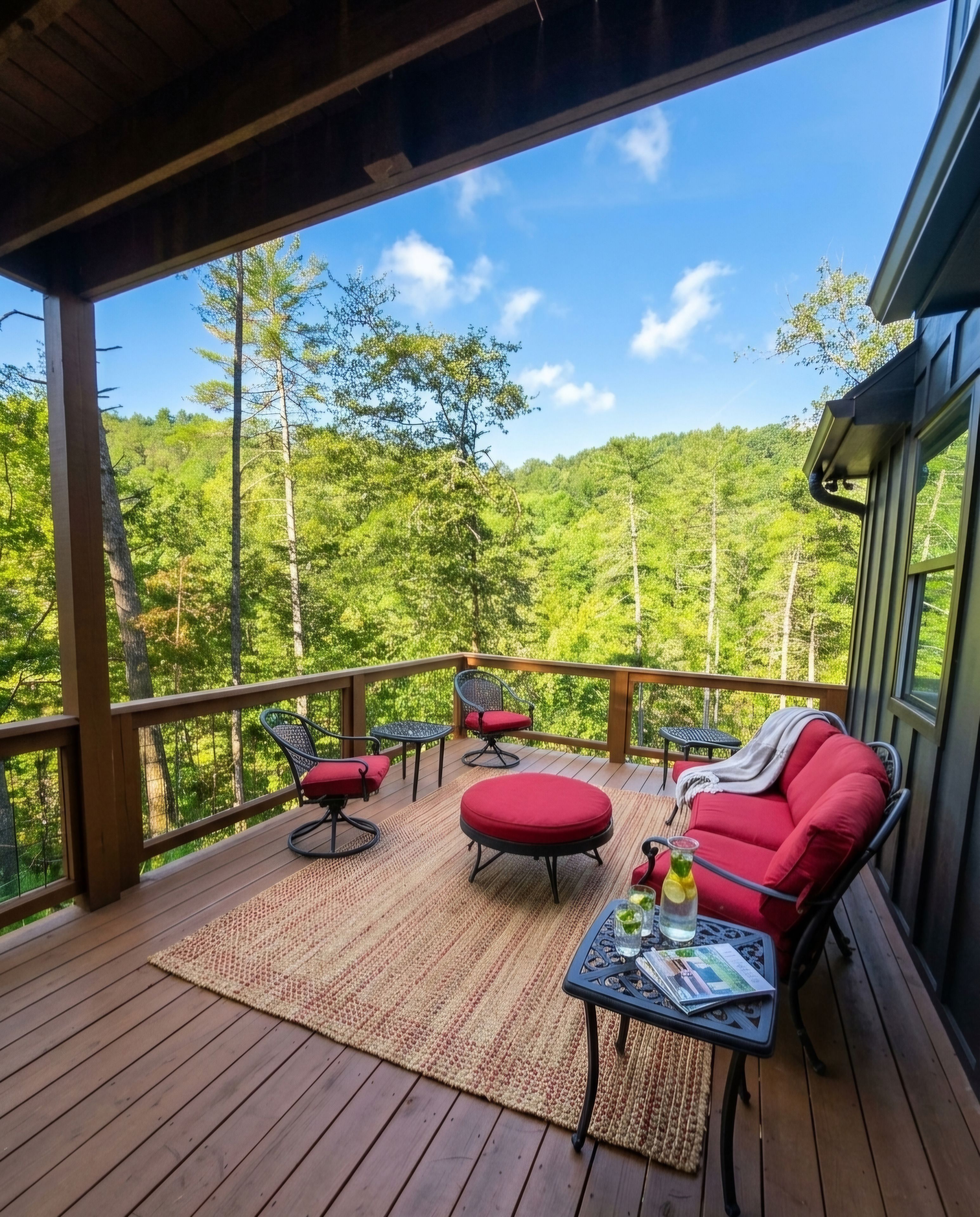 A covered outdoor deck with wooden flooring, red cushioned seating, and a table with drinks.