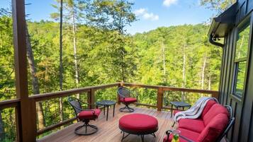 A covered outdoor deck with wooden flooring, red cushioned seating, and a table with drinks.