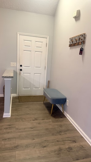 A room with a white door, a small bench, a wall-mounted key holder, and a textured ceiling.