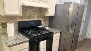 A kitchen with a stainless steel refrigerator, a black stove, and a granite countertop.