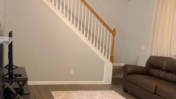 A living room with a wooden staircase, a ceiling fan, a brown sofa, and a patterned rug.