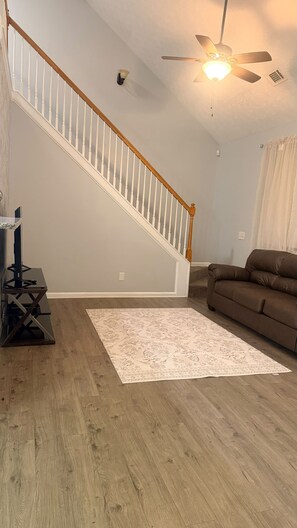 A living room with a wooden staircase, a ceiling fan, a brown sofa, and a patterned rug.
