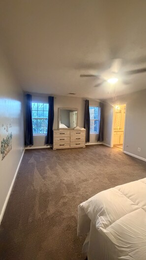 A bedroom with a large bed, a dresser, and two windows with curtains.