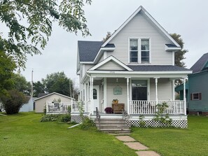 Une maison à deux étages avec un porche, une porte d’entrée et un petit jardin devant.