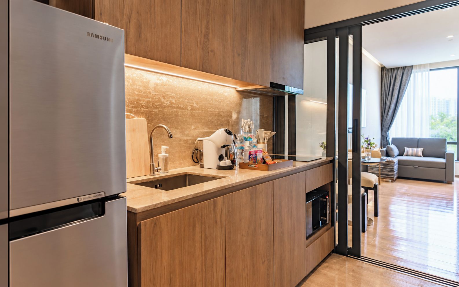 A modern kitchen with a stainless steel refrigerator, wooden cabinets, a double sink, and a coffee machine.