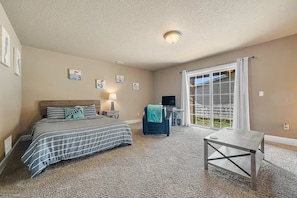 A bedroom with a bed, a desk, a chair, a TV, and a sliding glass door leading to a balcony. - Ocean-View Coastal Retreat | Walk to Beach | Garage + EV Charging (Rockaway Beach)