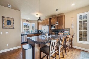 A kitchen with wooden cabinets, a granite countertop, and a central island with bar stools. - Ocean-View Coastal Retreat | Walk to Beach | Garage + EV Charging (Rockaway Beach)