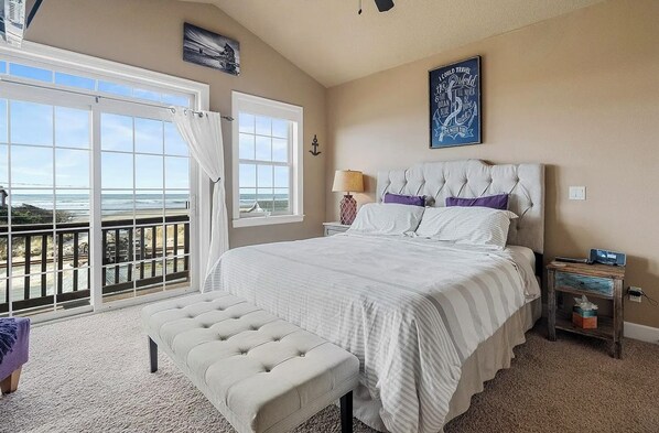 A bedroom with a large bed, a bench, a nightstand, and a view of the ocean. - Ocean-View Coastal Retreat | Walk to Beach | Garage + EV Charging (Rockaway Beach)