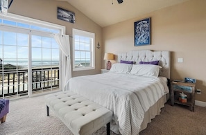 A bedroom with a large bed, a bench, a nightstand, and a view of the ocean. - Ocean-View Coastal Retreat | Walk to Beach | Garage + EV Charging (Rockaway Beach)