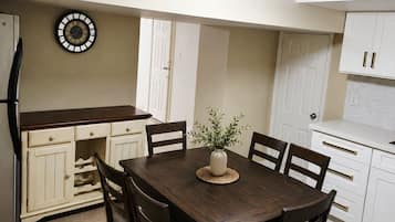 A kitchen with a dining table, chairs, cabinets, a clock, and a refrigerator.