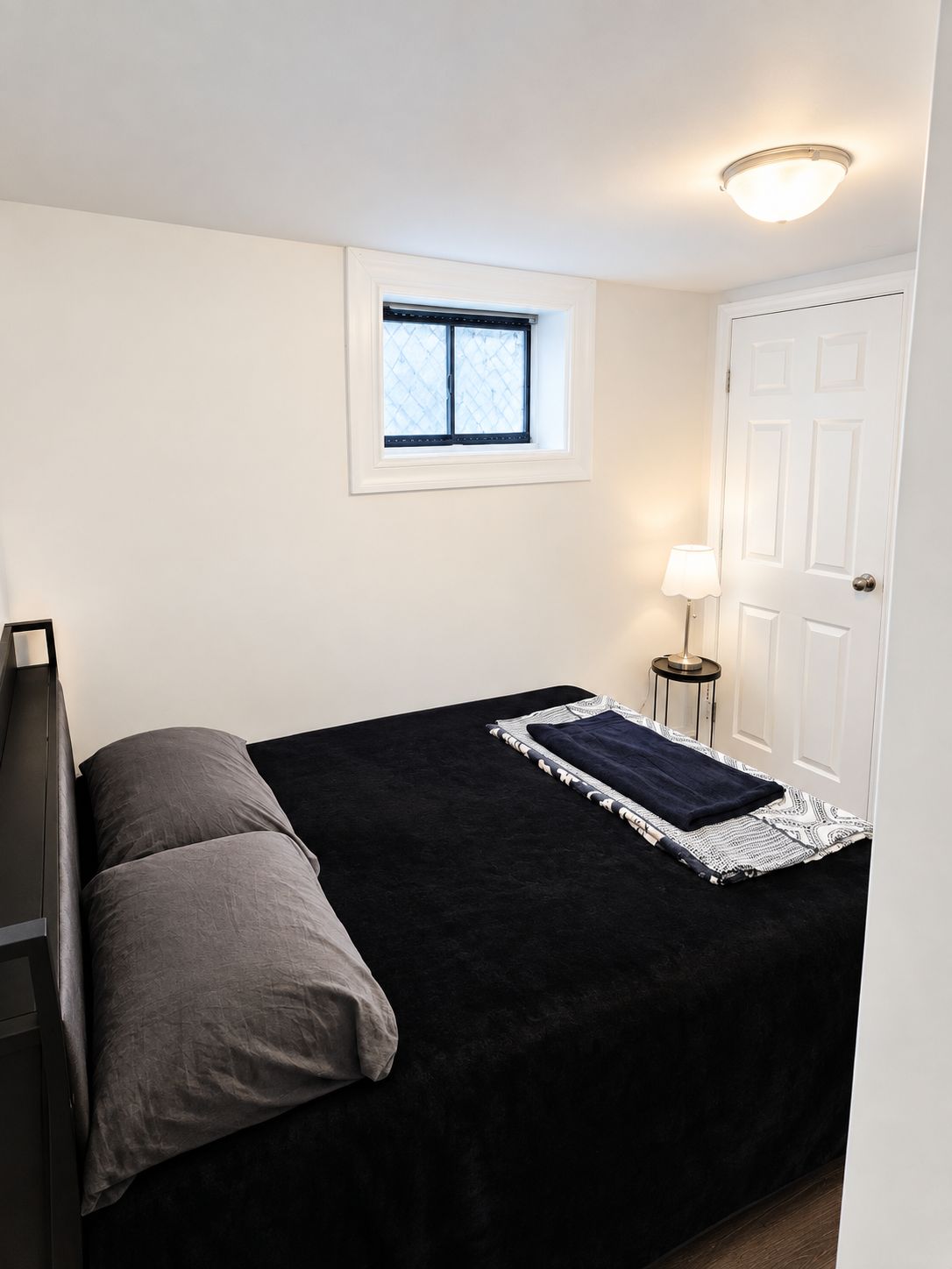 A bedroom with a bed, a window, a door, and a bedside lamp.