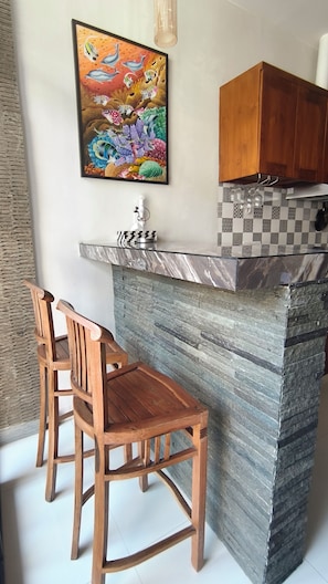 A kitchen with a marble countertop, wooden chairs, and a colorful painting on the wall. - Oriana Canggu 3-Bedroom Villa with Private Pool (Badung)