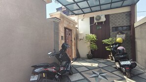 Un patio con dos motocicletas estacionadas, piso de baldosas, una puerta de madera y una pequeña planta en maceta.