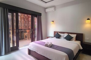 Habitación de hotel con cama, mesita de noche, aire acondicionado instalado en la pared y puerta corrediza de vidrio que da a un área exterior.