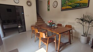 A dining area with a wooden table and chairs, a staircase, and a painting on the wall. - Oriana Canggu 3-Bedroom Villa with Private Pool (Badung)