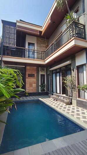 A two-story house with a swimming pool, stone walls, and a balcony with a railing. - Oriana Canggu 3-Bedroom Villa with Private Pool (Badung)