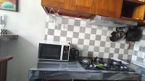A kitchen with a microwave, gas stove, and a checkered backsplash. - Oriana Canggu 3-Bedroom Villa with Private Pool (Badung)