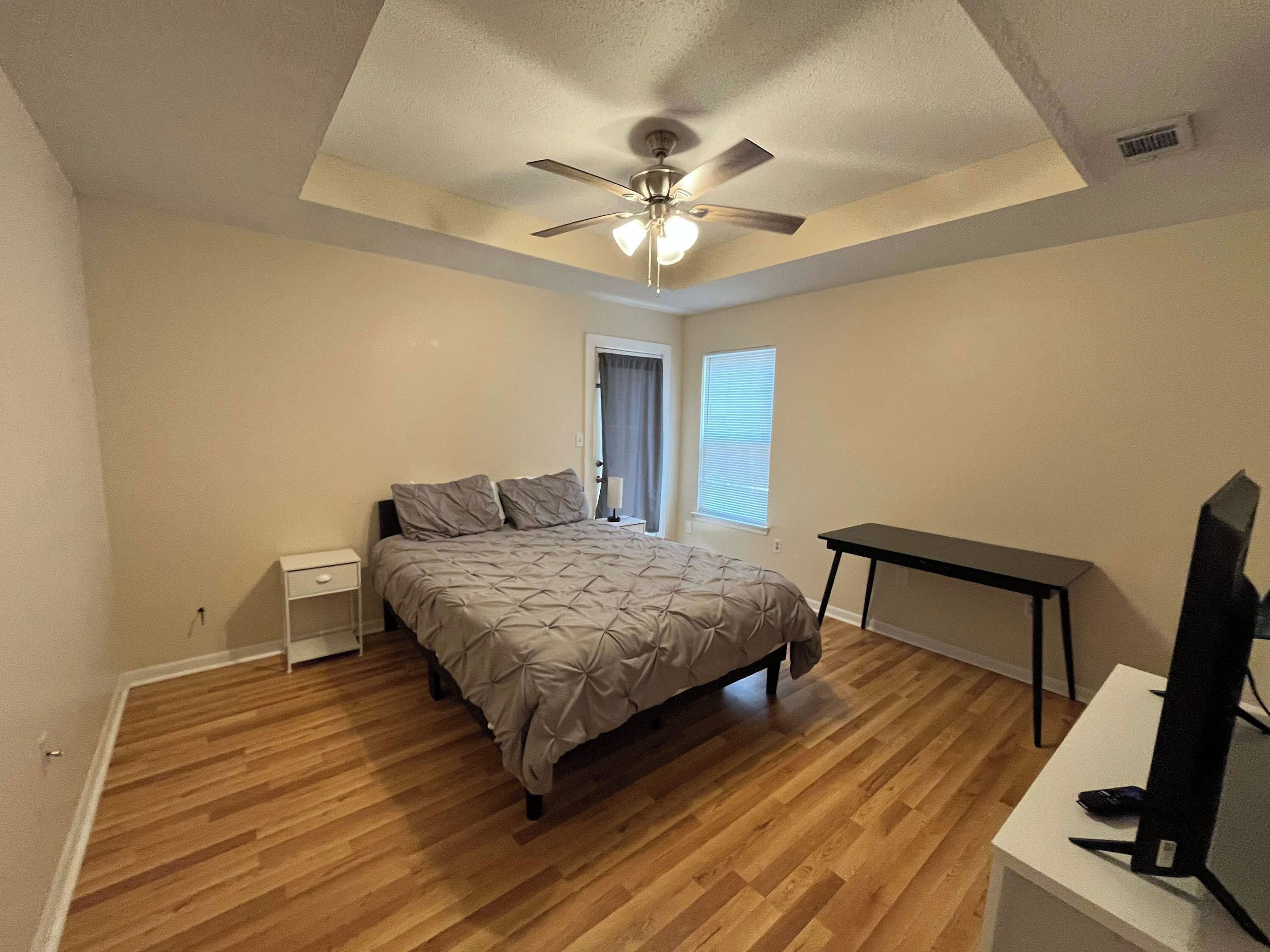 Une chambre à coucher avec un lit, un bureau, un ventilateur de plafond et une fenêtre.