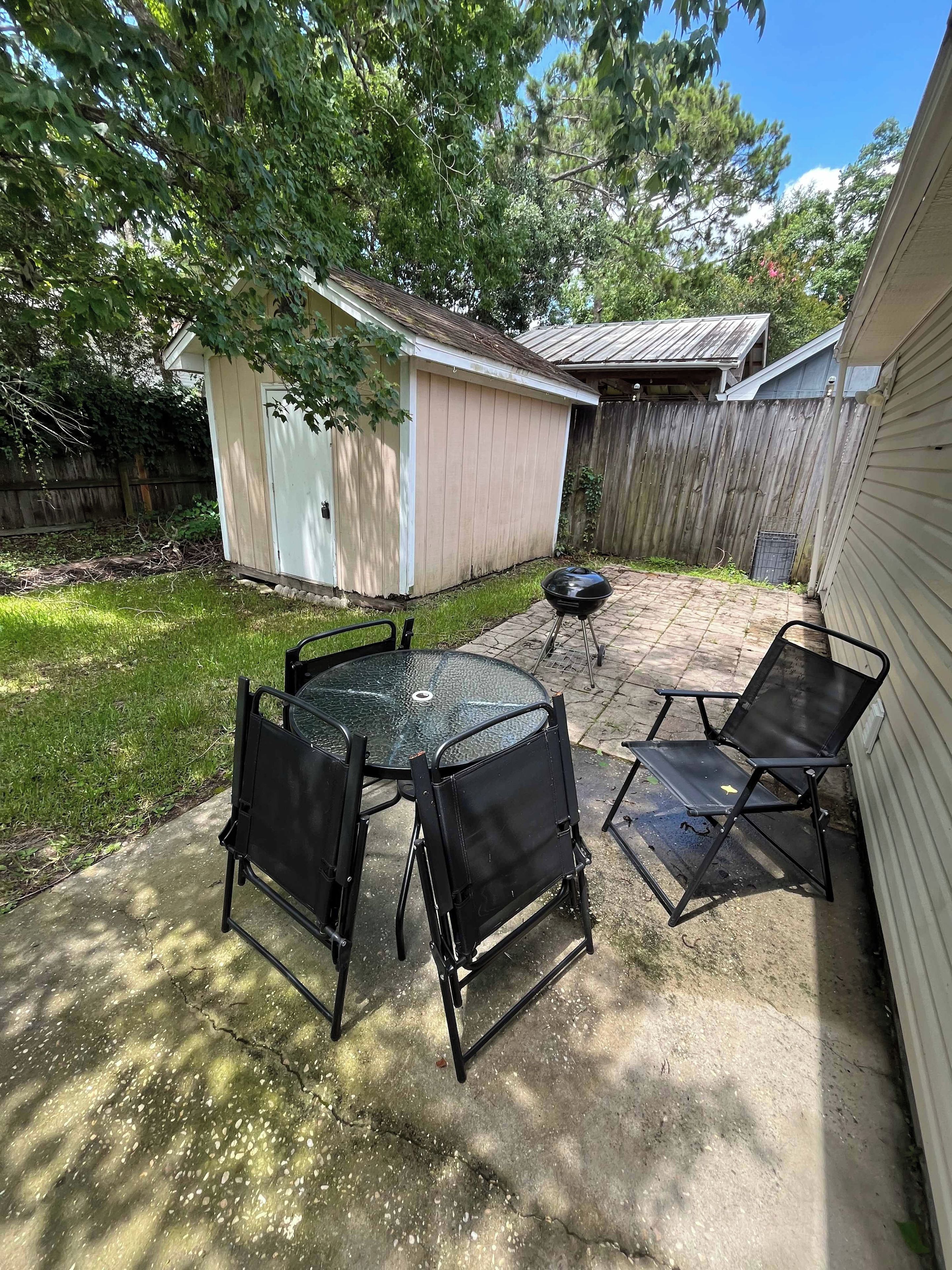 A backyard with a patio table and chairs, a barbecue grill, and a shed.