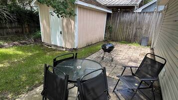 A backyard with a patio table and chairs, a barbecue grill, and a shed.