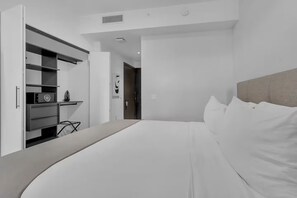 A modern bedroom with a large bed, a wardrobe with a microwave, and a door leading to another room. - High-Floor Studio| Rooftop Pool + Beach Club | Downtown Miami (Miami)