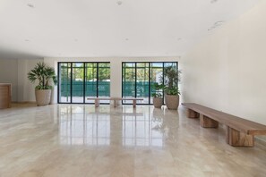 A spacious room with a large window, a bench, and potted plants.