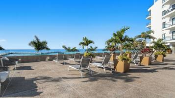A rooftop terrace with lounge chairs and potted plants, overlooking a pool and ocean view.
