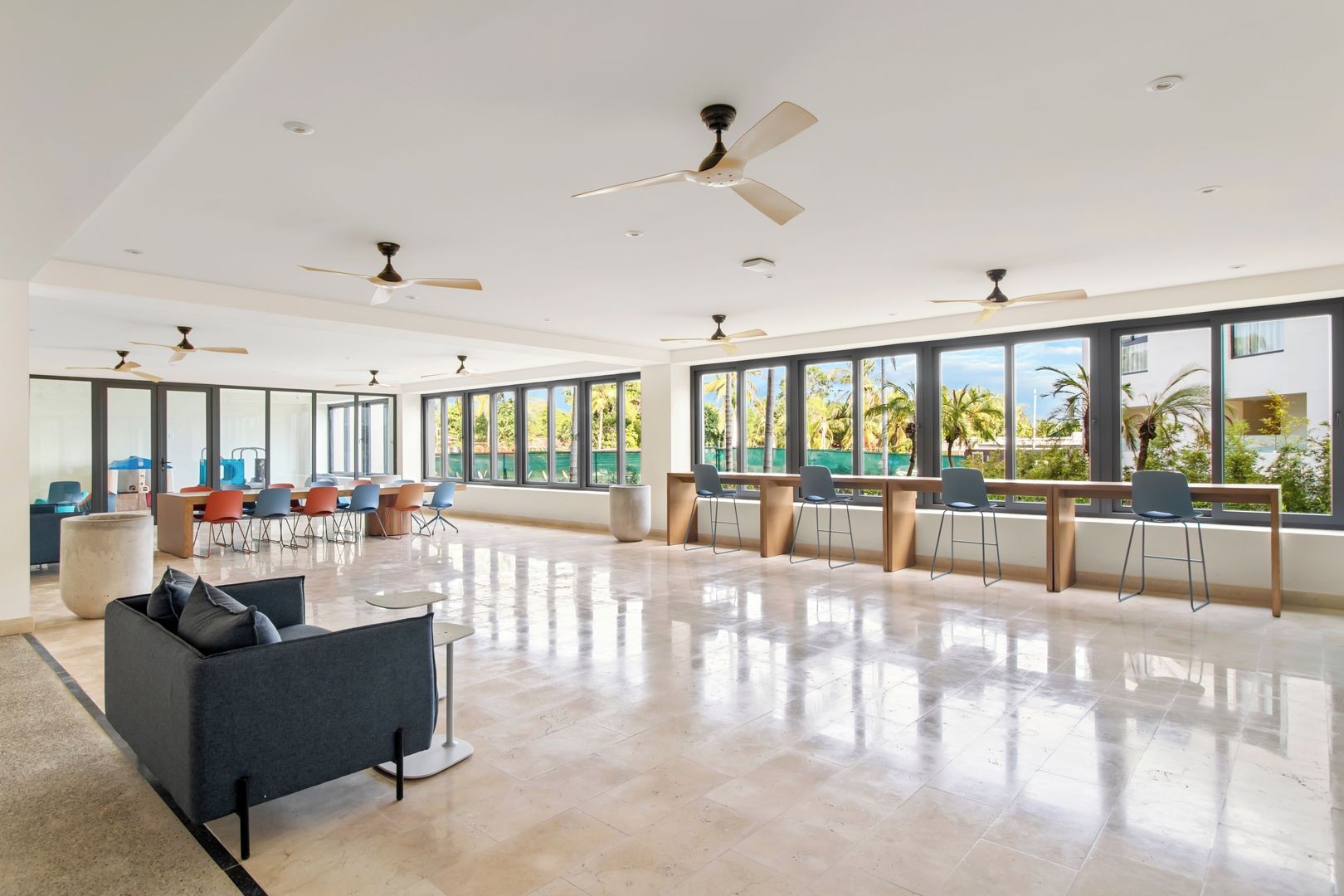 A spacious room with a large window, a ceiling fan, and a seating area with chairs and a sofa.