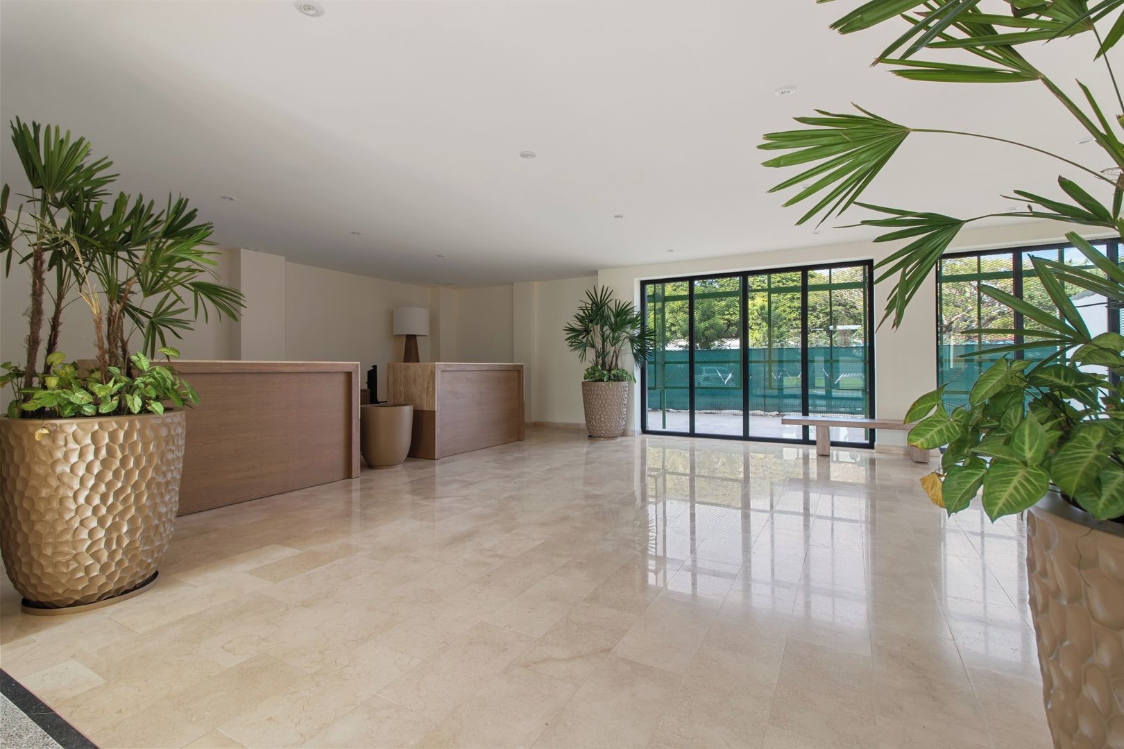 A spacious lobby with a reception desk, potted plants, and a large window offering a view of the outdoors.