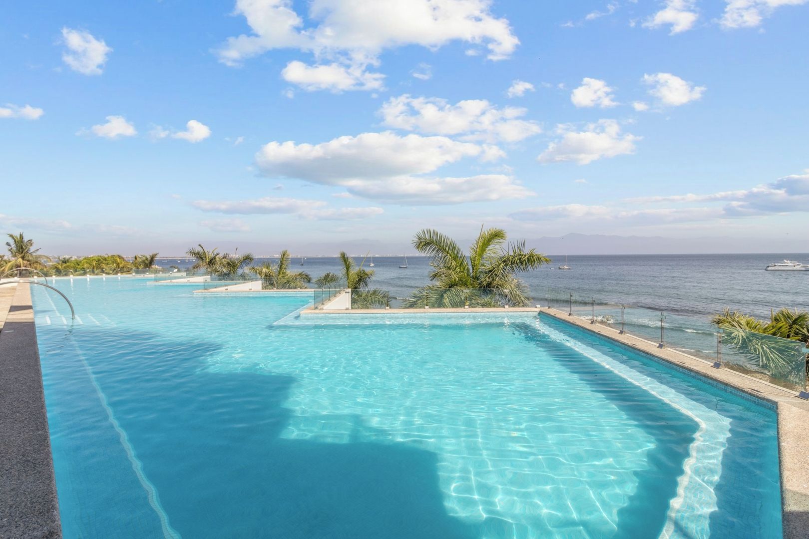 A pool with clear blue water, surrounded by palm trees and a view of the ocean.