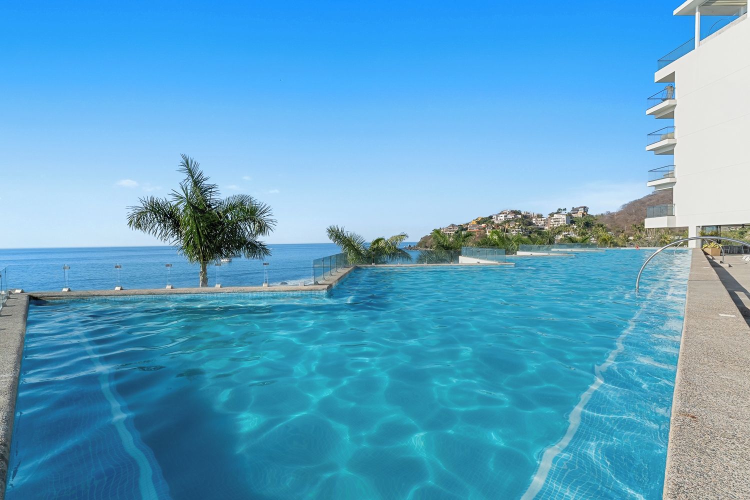 Une piscine d’un bleu éclatant, avec vue sur l’océan et un bâtiment en arrière-plan.