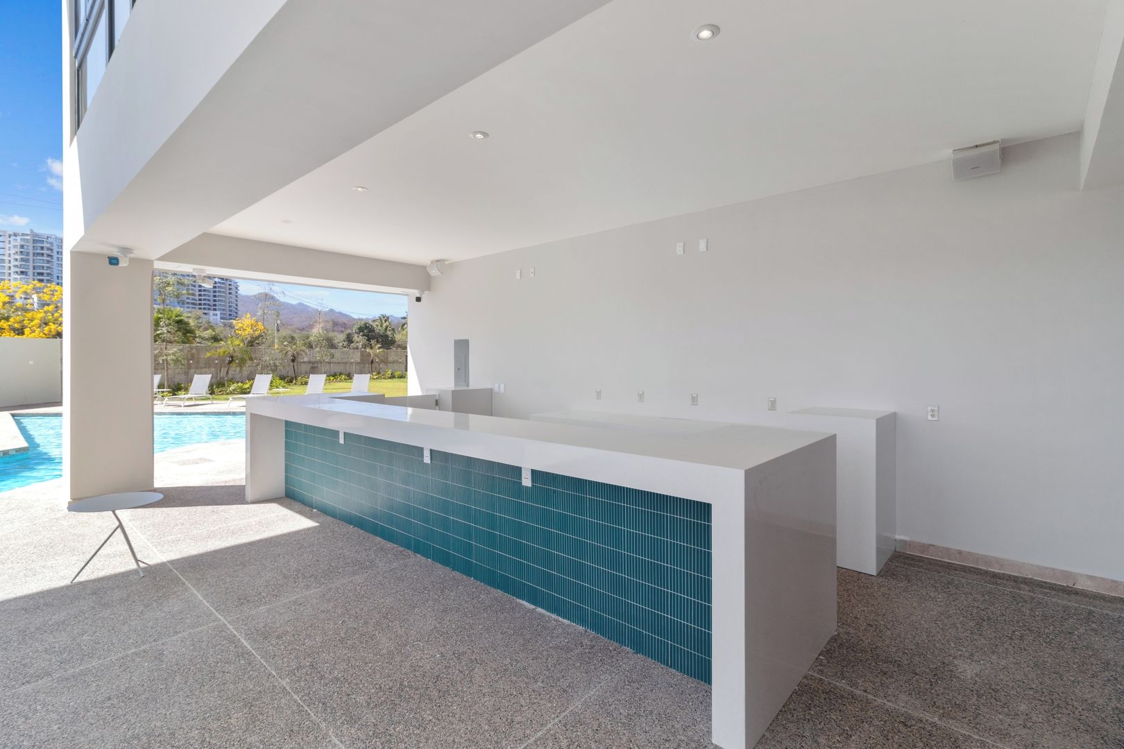 A modern outdoor kitchen area with a pool and lounge chairs, featuring a clean, minimalist design.