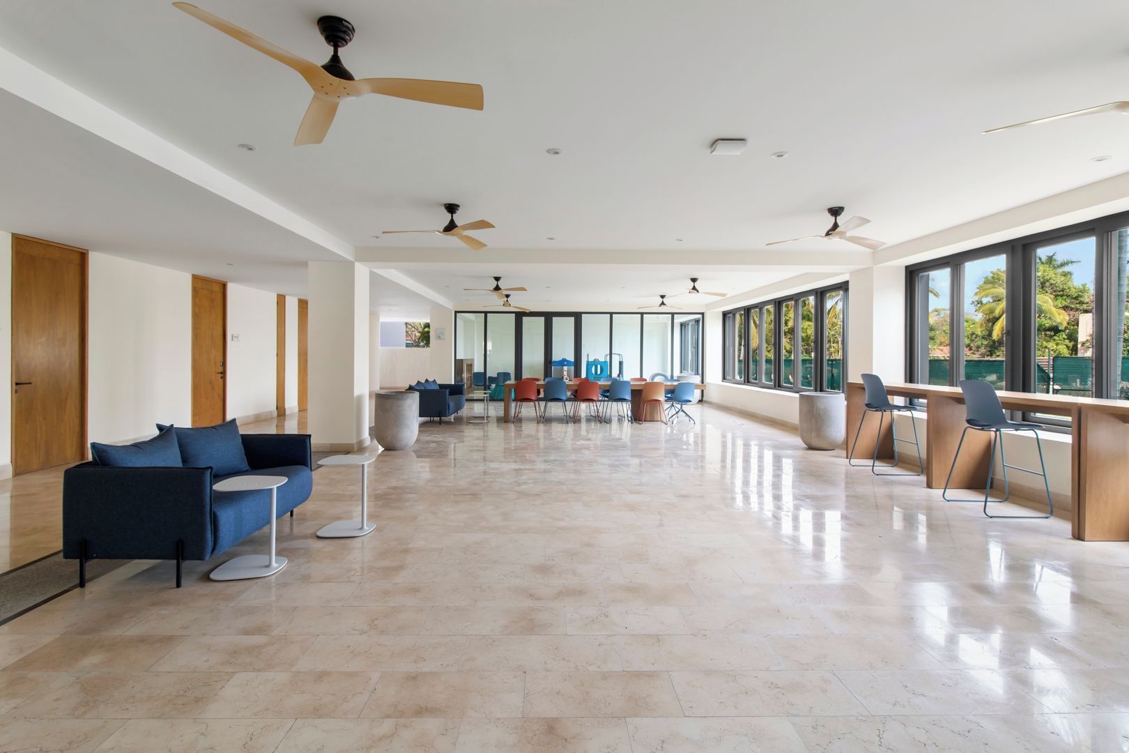 A spacious indoor area with multiple seating arrangements, ceiling fans, and large windows offering views.