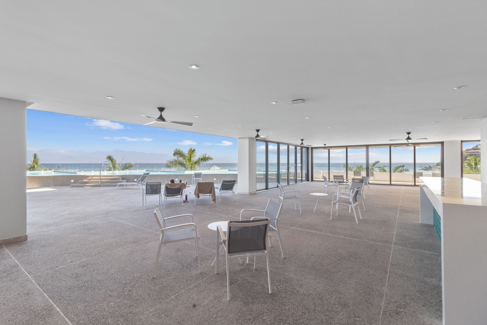 A spacious outdoor terrace with a view of the ocean, furnished with chairs and tables.