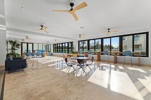A spacious indoor area with multiple ceiling fans, large windows, and a variety of seating arrangements including tables and chairs.