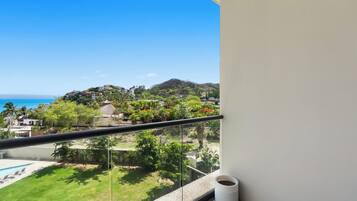 A balcony with a clear view of a beach, a pool, and a lush green landscape.