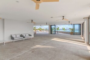 A spacious indoor area with a ceiling fan, a sofa, and a view of a pool and ocean.