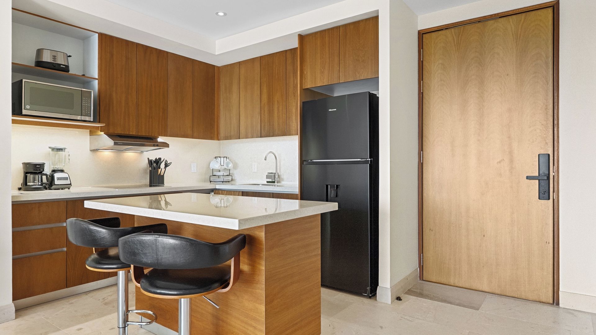 A modern kitchen with wooden cabinets, a black refrigerator, a bar stool, and a coffee maker.