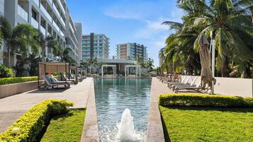 A hotel pool area with a fountain, lounge chairs, and palm trees.