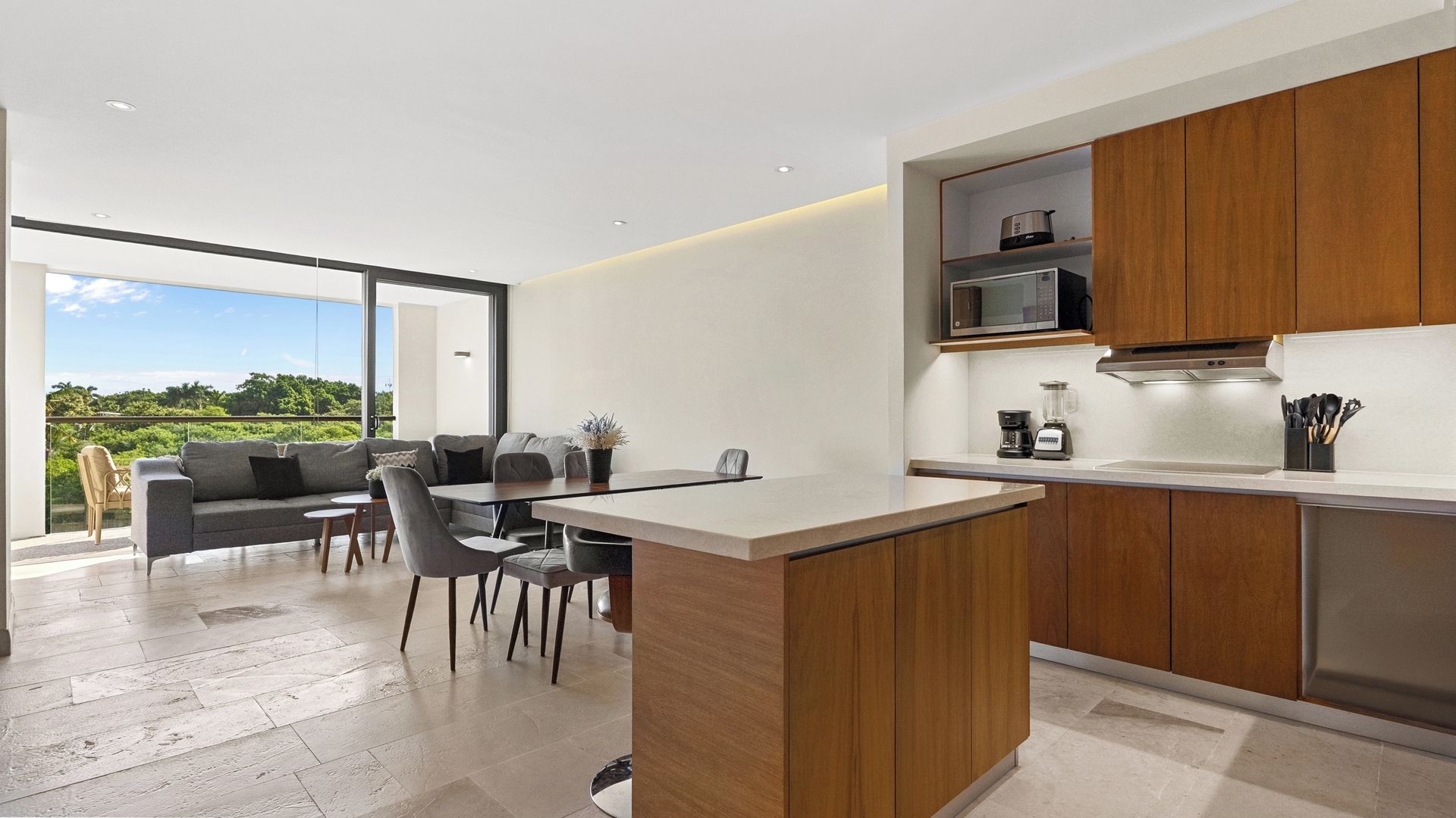A modern kitchen with a dining area, wooden cabinets, and a view of greenery.