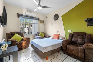 Ein Zimmer mit einem Bett, zwei Sesseln, einem kleinen Tisch und einem Deckenventilator.