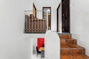 Eine Treppe mit weißer Brüstung führt zu einem Balkon im zweiten Stock, der ein braunes Sofa und eine rote Wandzierde bietet.