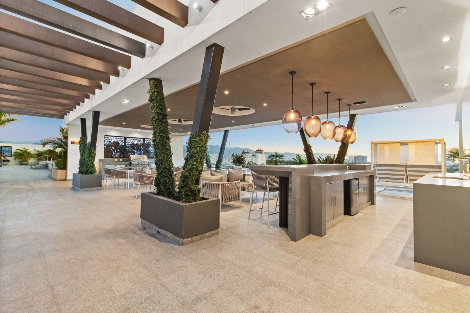 A modern outdoor lounge area with seating, a bar, and a view of the cityscape.