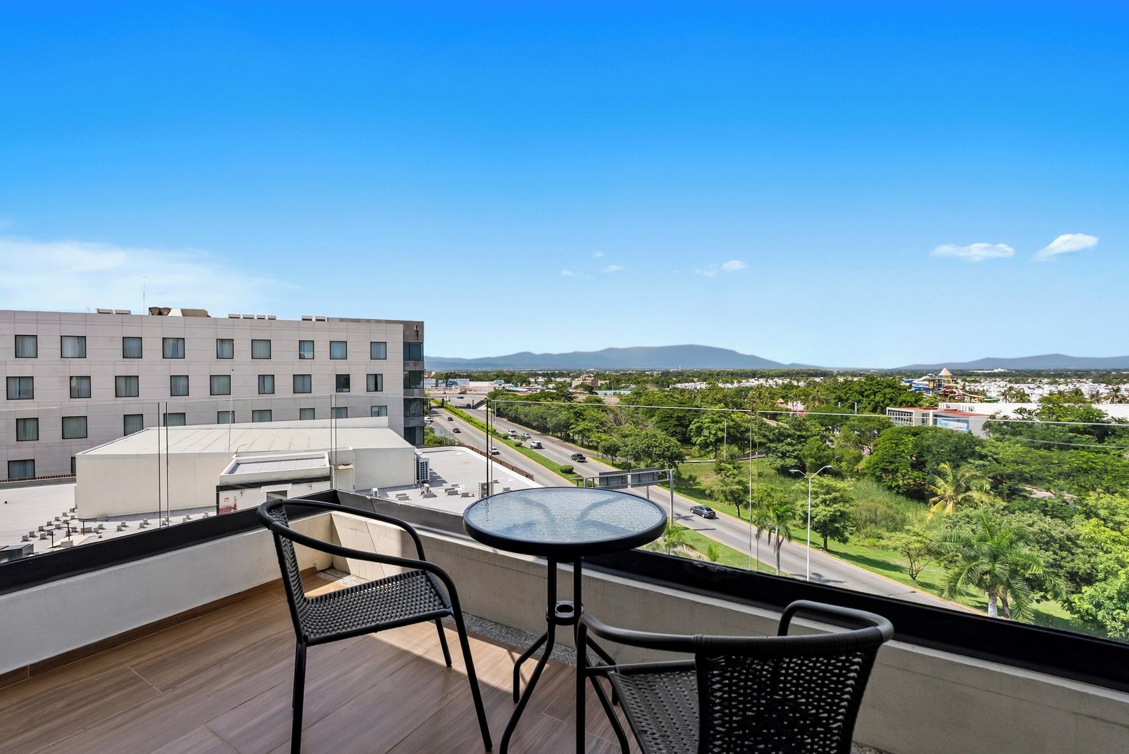 A balcony with a table and chairs overlooking a cityscape with buildings and greenery.