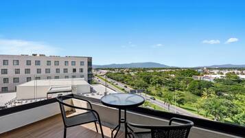 A balcony with a table and chairs overlooking a cityscape with buildings and greenery.