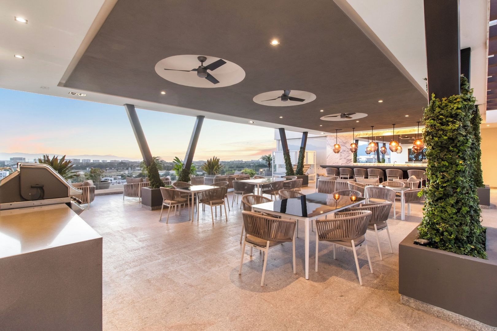 A rooftop bar with multiple seating areas, ceiling fans, and a view of the cityscape.