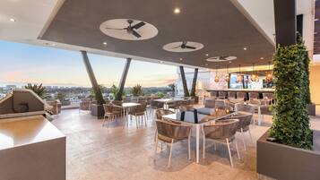A rooftop bar with multiple seating areas, ceiling fans, and a view of the cityscape.